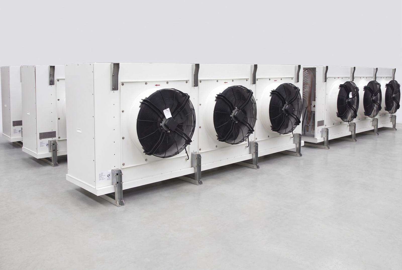 Row of industrial unit coolers with painted casings, large axial fans and stainless mounting brackets on a production floor.